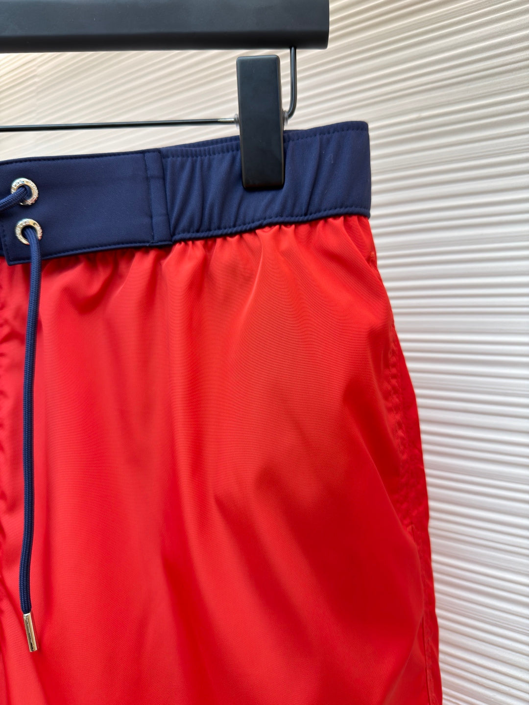 Red swim shorts front close-up with navy waistband and blue drawstring cord