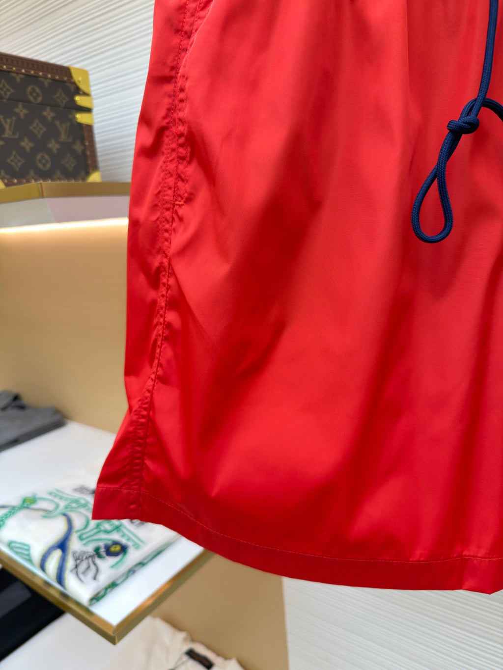 Red swim shorts lower side seam and pocket edge, hanging close-up