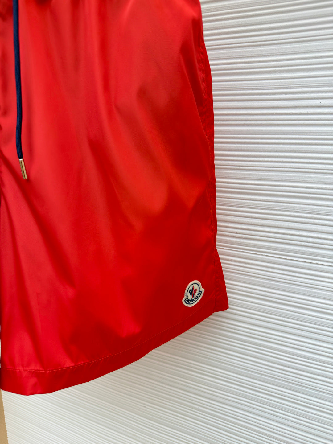 Red swim shorts hem with navy Moncler logo patch, side view