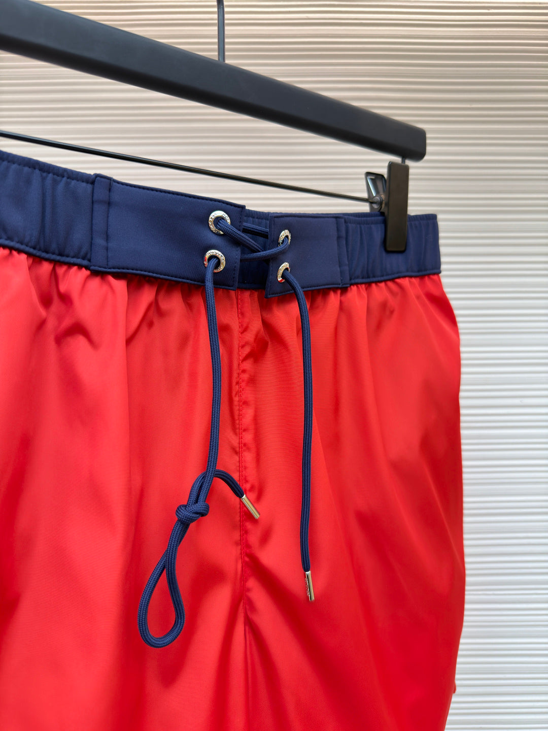 Red swim shorts waist close-up with navy drawstring and eyelets, hanging