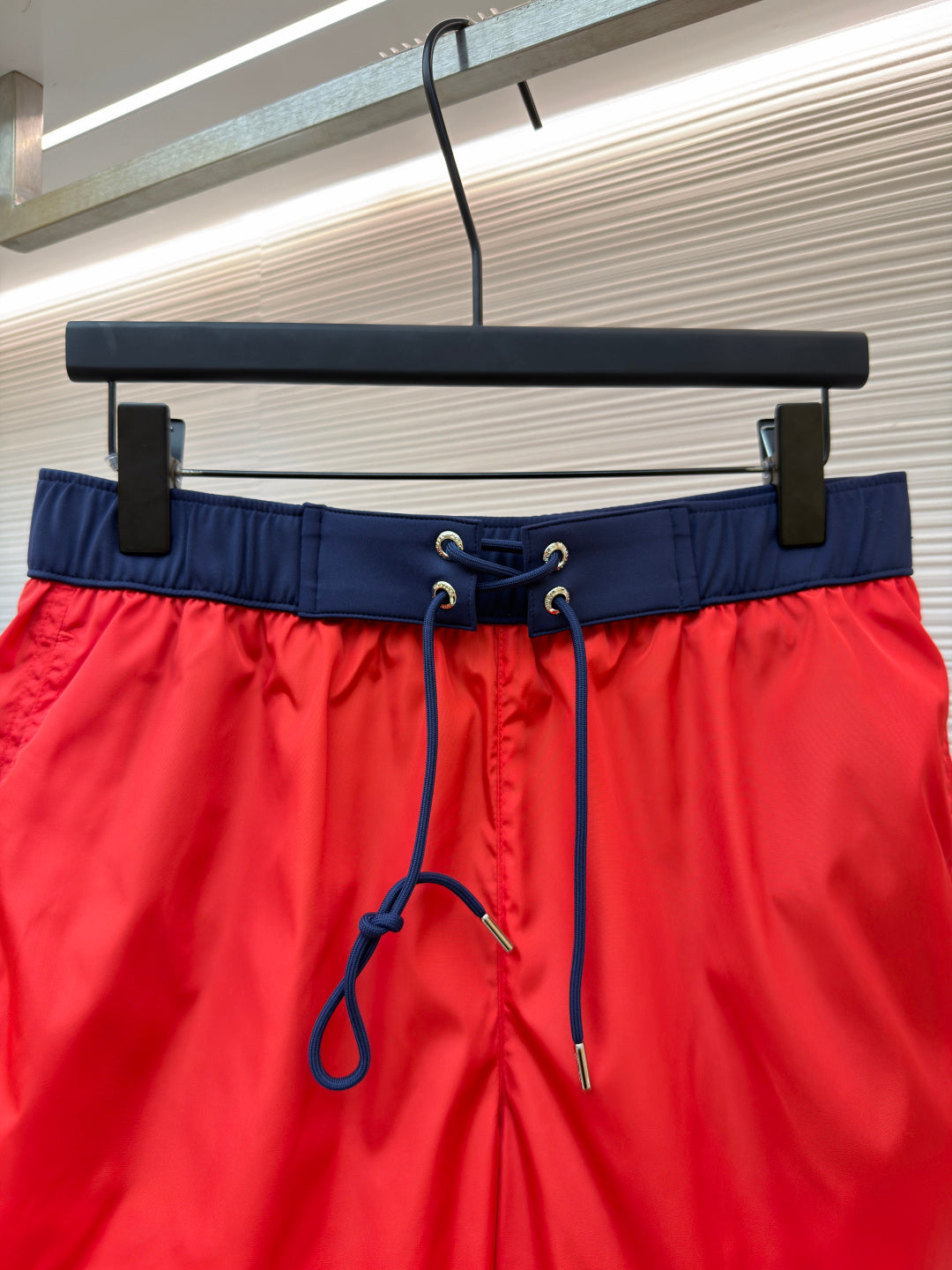 Red swim shorts waist close-up with navy elastic band and blue drawstring