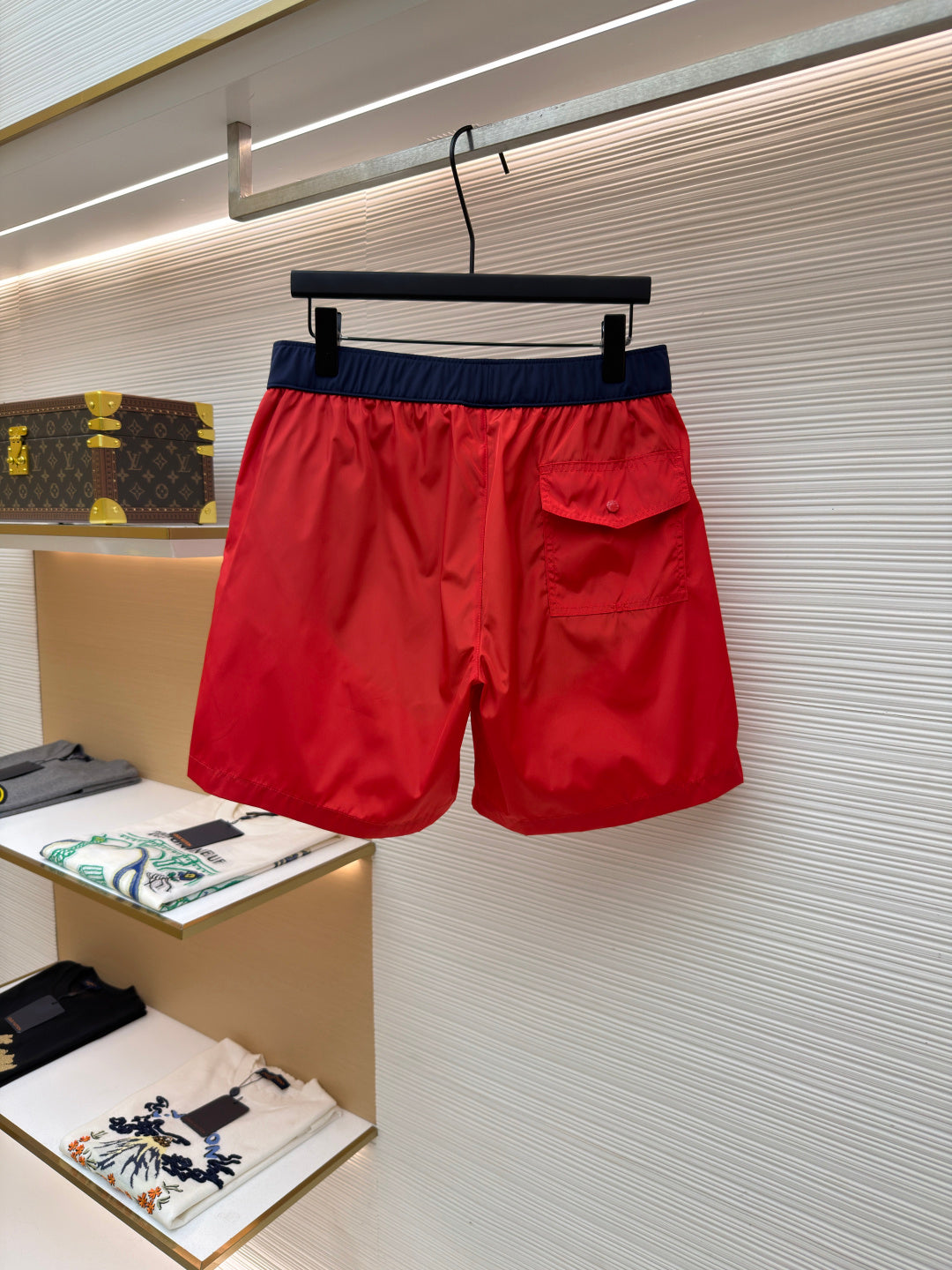 Red swim shorts with navy waistband and side pocket detail, hanging front view