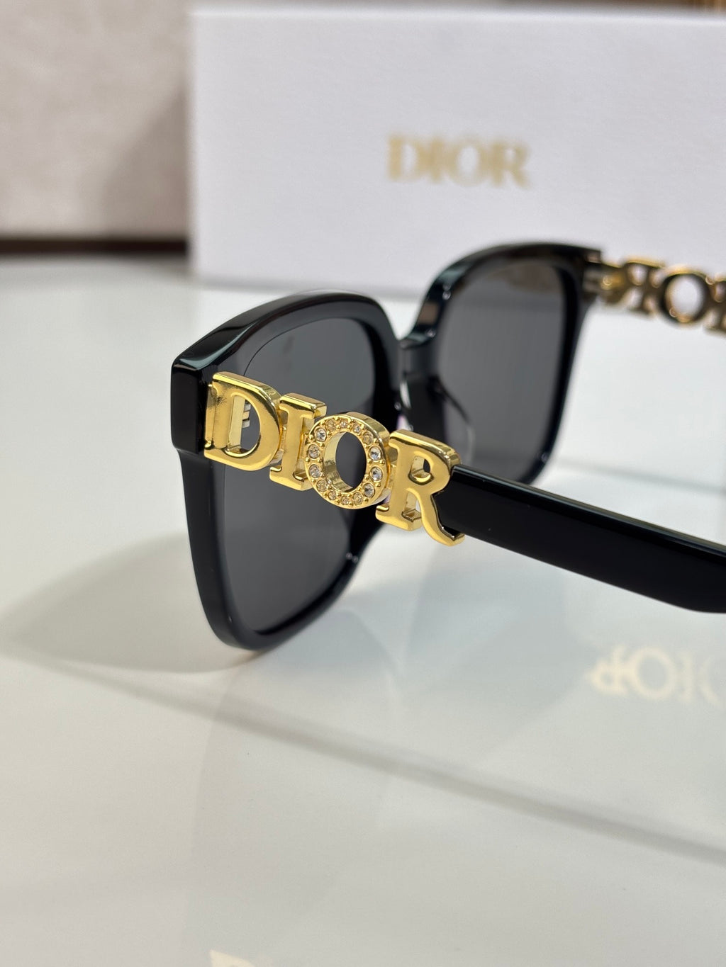 Black sunglasses close-up with gold logo emblem and dark lenses