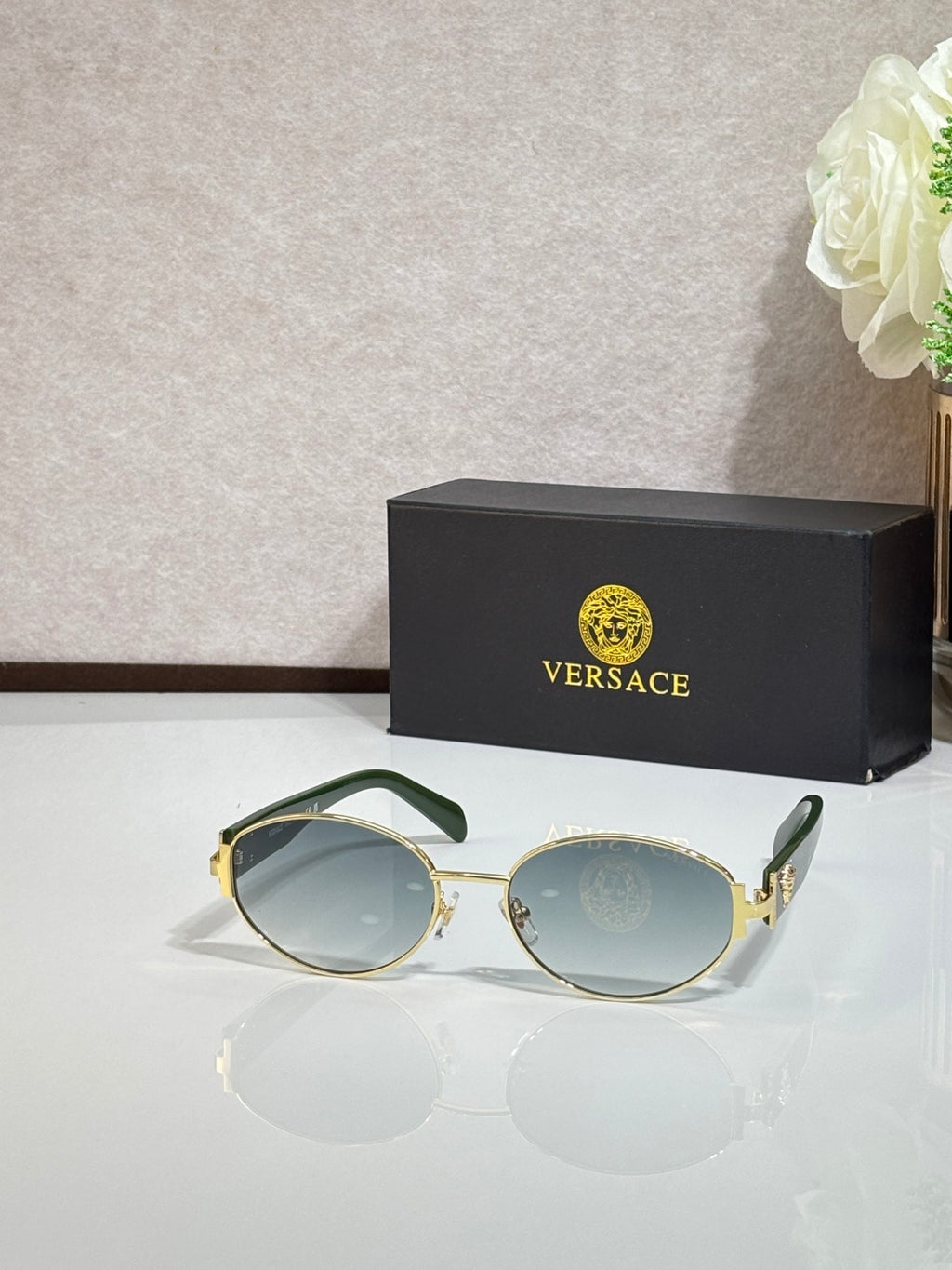 Round sunglasses with light blue lenses, gold-tone frame, and green temple accents