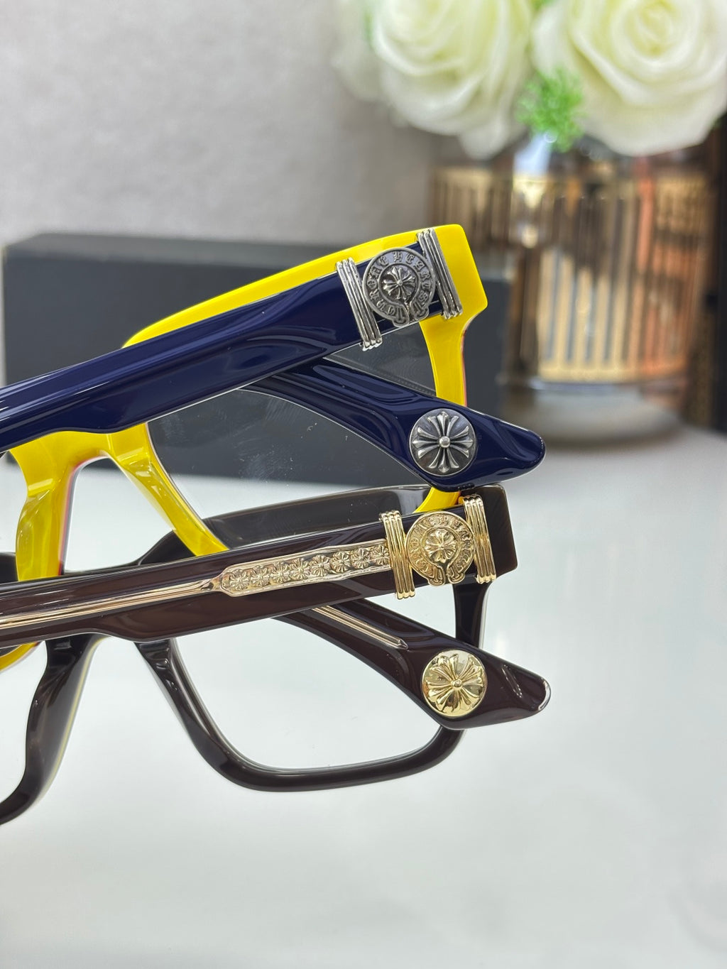 Color-block eyeglass frames with gold-tone decorative logos and clear lenses