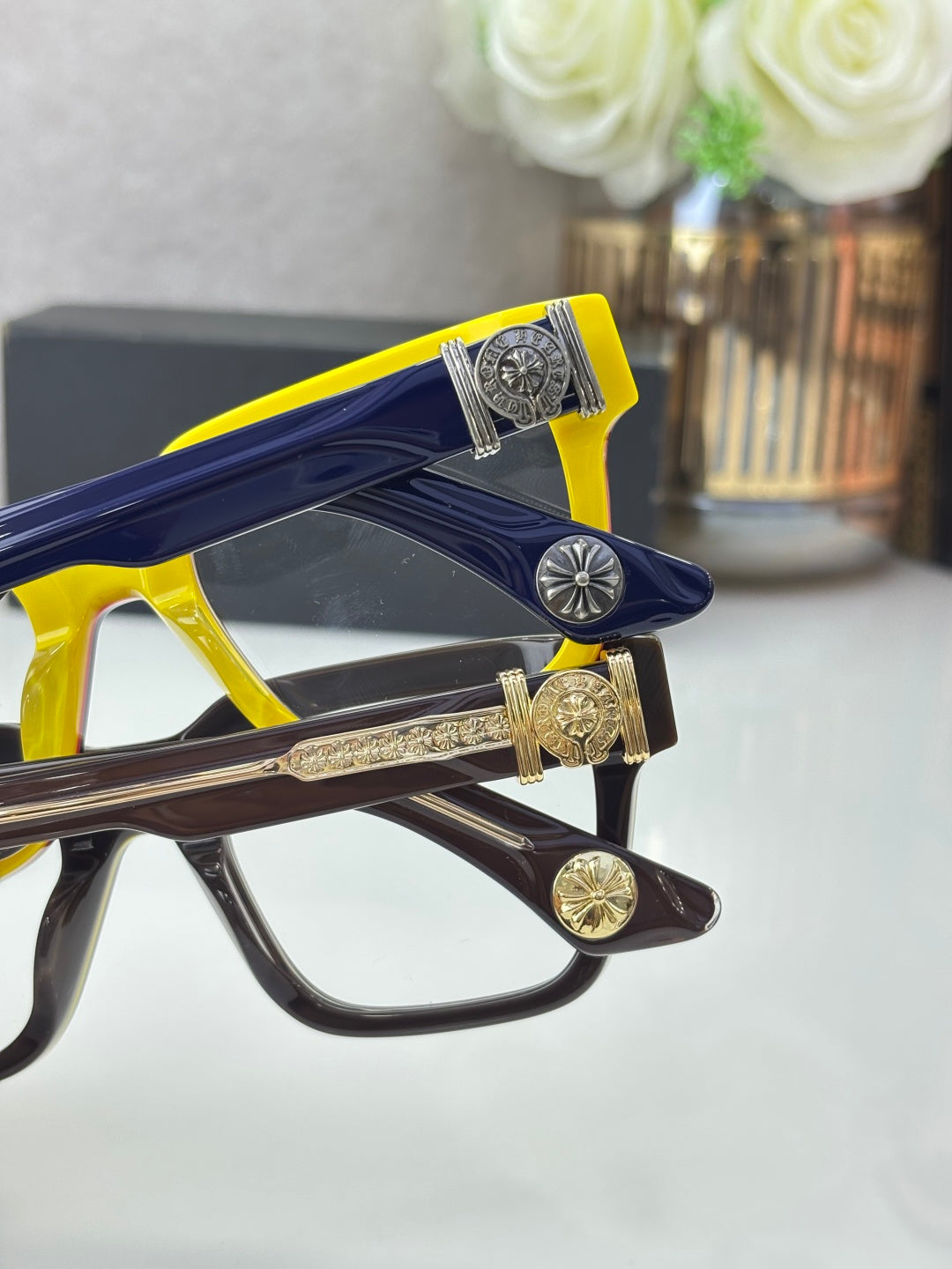 Color-block eyeglass frames with gold-tone decorative logos and clear lenses