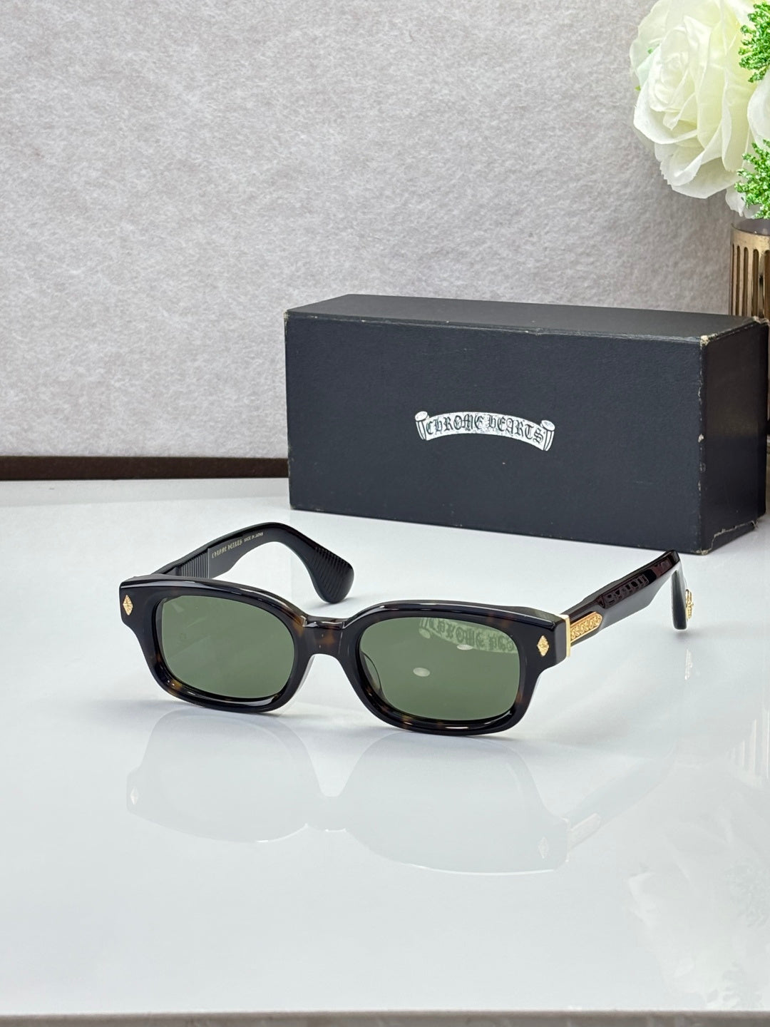 Black oval sunglasses with green-tinted lenses and gold temple detail