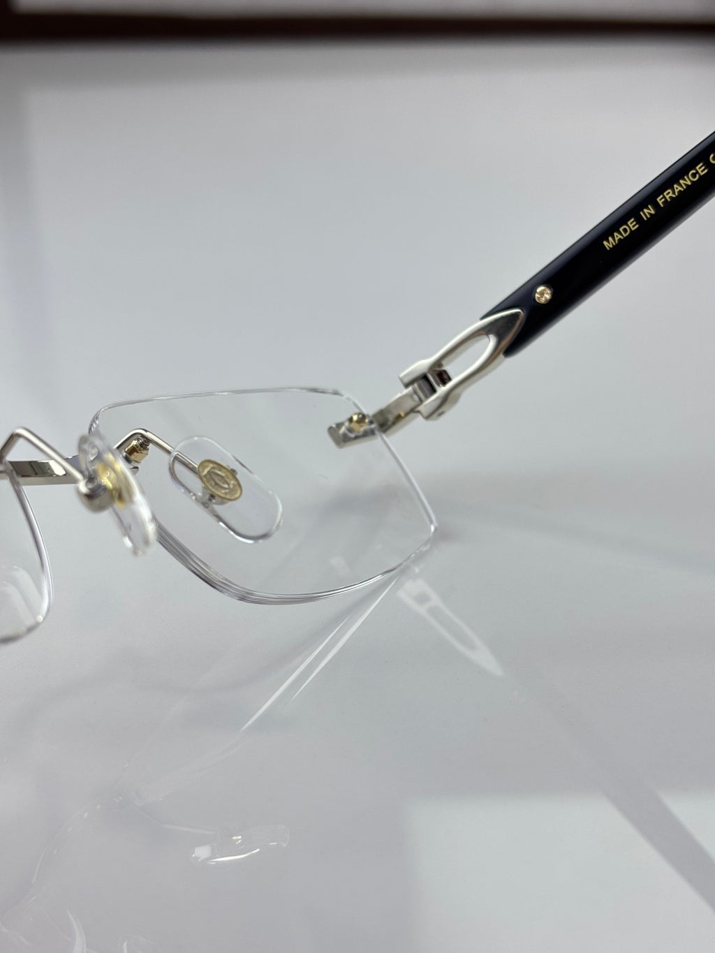 Clear eyeglasses close-up: black temple with small gold text and metal hinge detail.