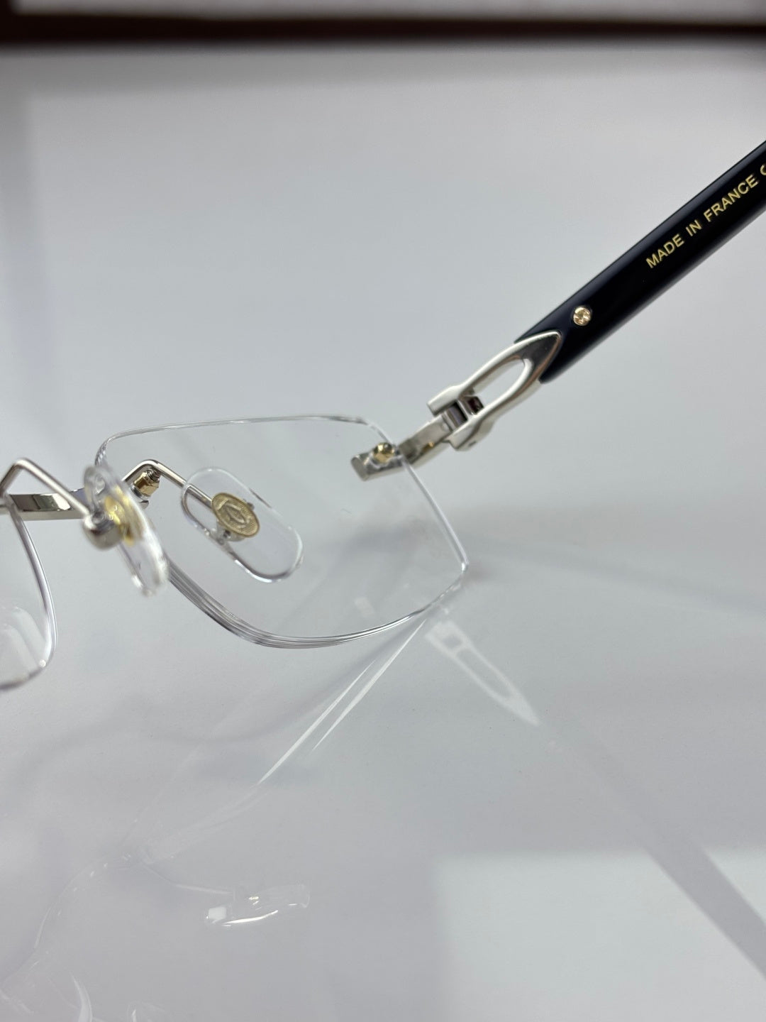 Clear eyeglasses close-up: black temple with small gold text and metal hinge detail.