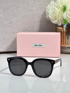 Black round sunglasses with dark gray lenses and gold logo accents on temples