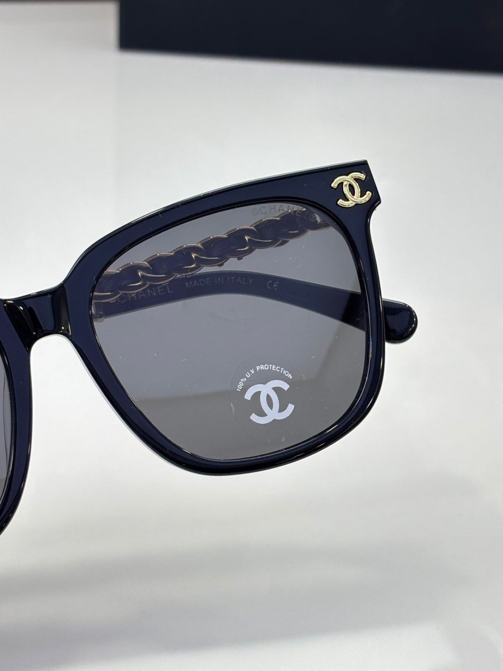 Chanel sunglasses close-up with dark blue frame, dark lenses, and gold logo emblem