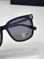 Chanel sunglasses close-up with dark blue frame, dark lenses, and gold logo emblem