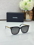 Chanel sunglasses with black frames, dark lenses, and gold chain detail on the temples