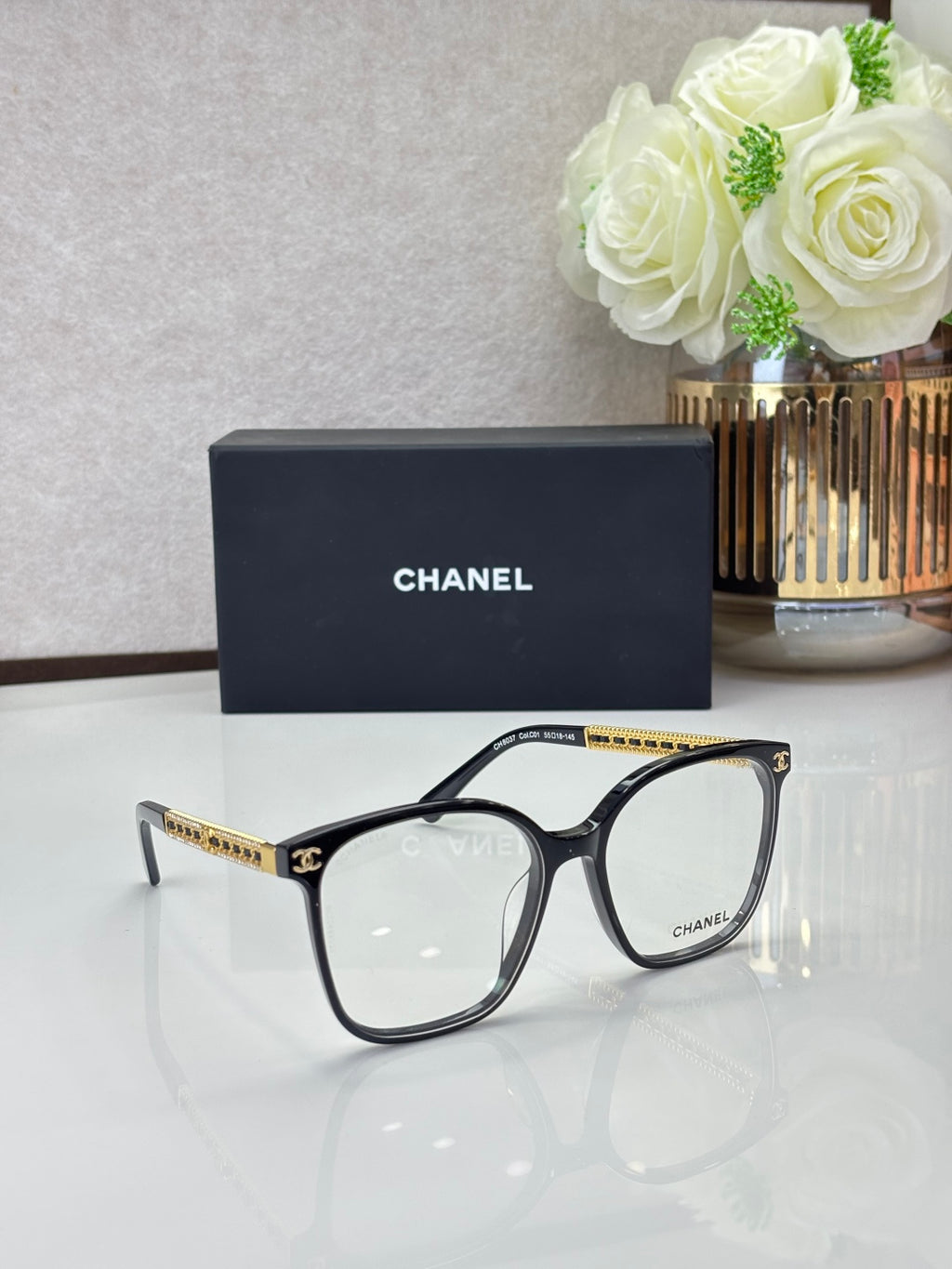 Chanel eyeglasses with black square frames and clear lenses, gold-tone logo temples
