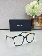 Chanel eyeglasses with black square frames and clear lenses, gold-tone logo temples