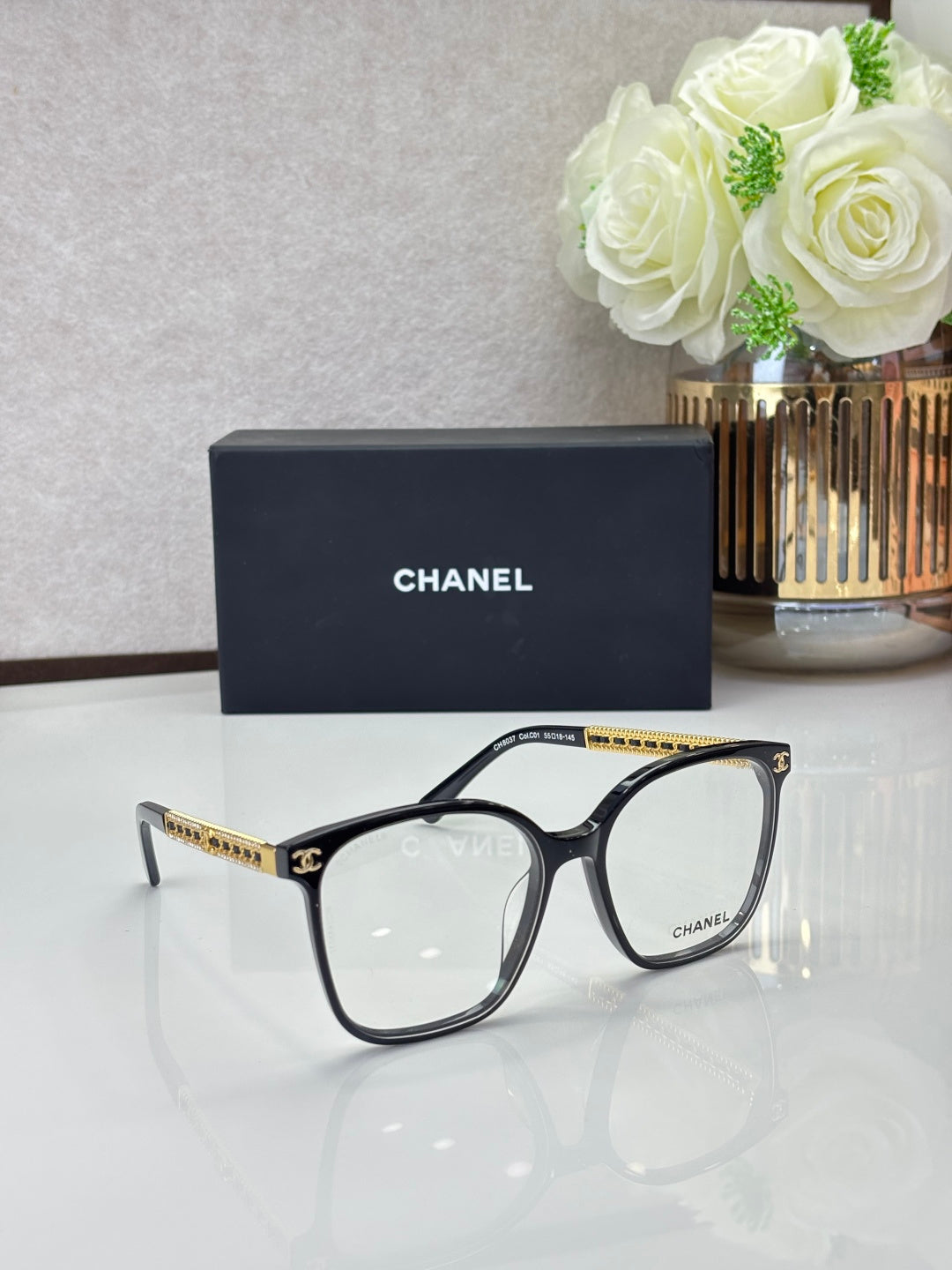 Chanel eyeglasses with black square frames and clear lenses, gold-tone logo temples