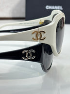 White sunglasses close-up with gold CC emblem on temple and dark lens