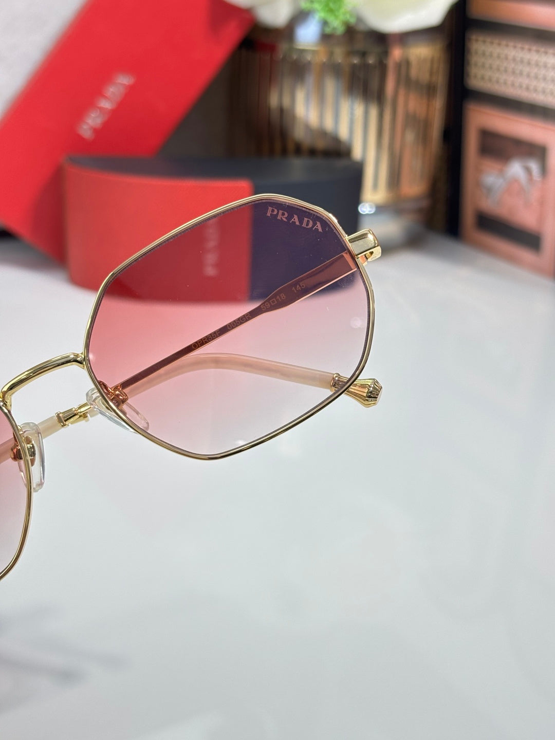 Prada sunglasses close-up with gold-tone frame and pink gradient tinted lens