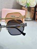 Close-up: gold square sunglasses with dark lenses and Miu Miu logo on the temples