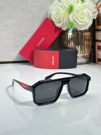 Rectangular black sunglasses with dark lenses and red Prada branding on temples