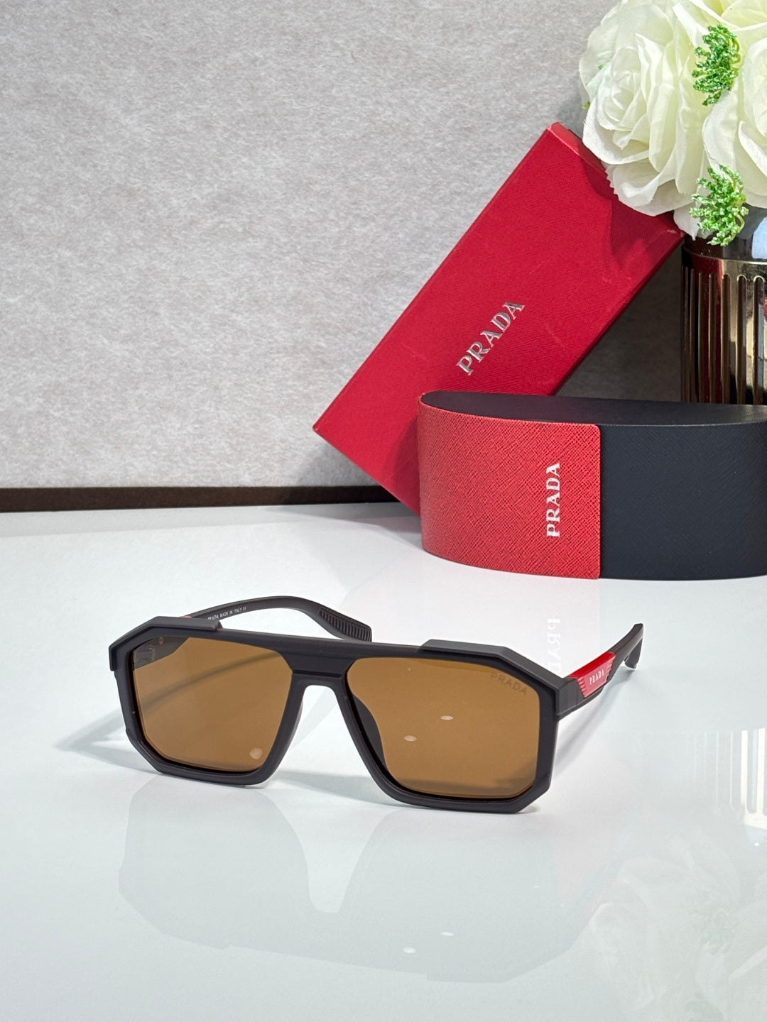 Rectangular black sunglasses with brown-tinted lenses and Prada logo at temple
