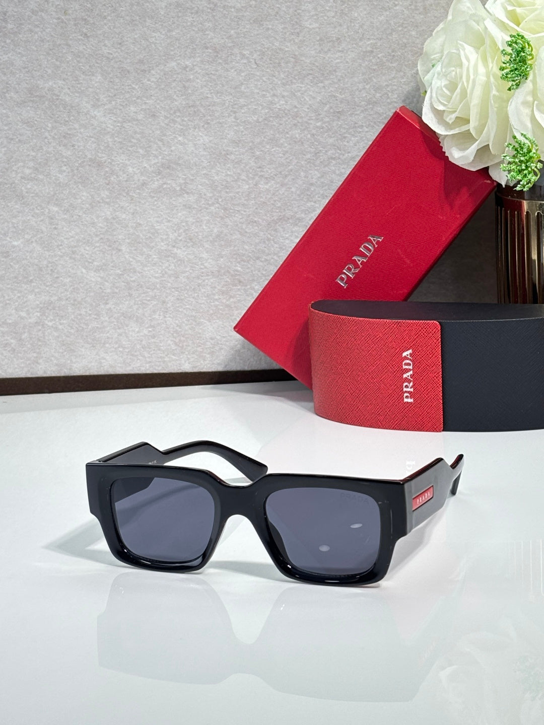 Black square sunglasses with dark lenses and Prada branding on the temple