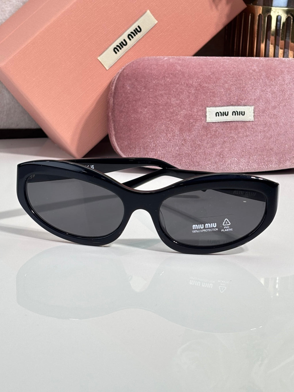 Black sunglasses with dark lenses; pink hard case and purple glasses pouch