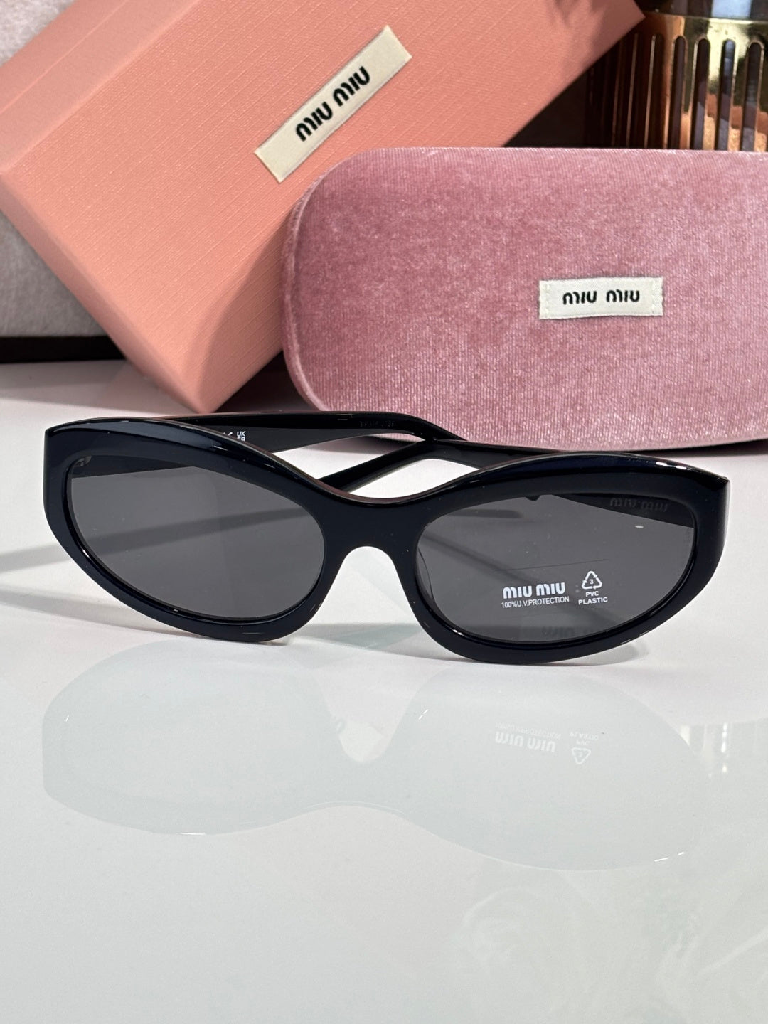 Black sunglasses with dark lenses; pink hard case and purple glasses pouch