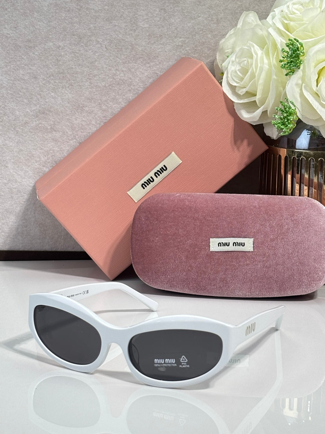 White sunglasses with dark lenses; pink hard case and purple glasses pouch
