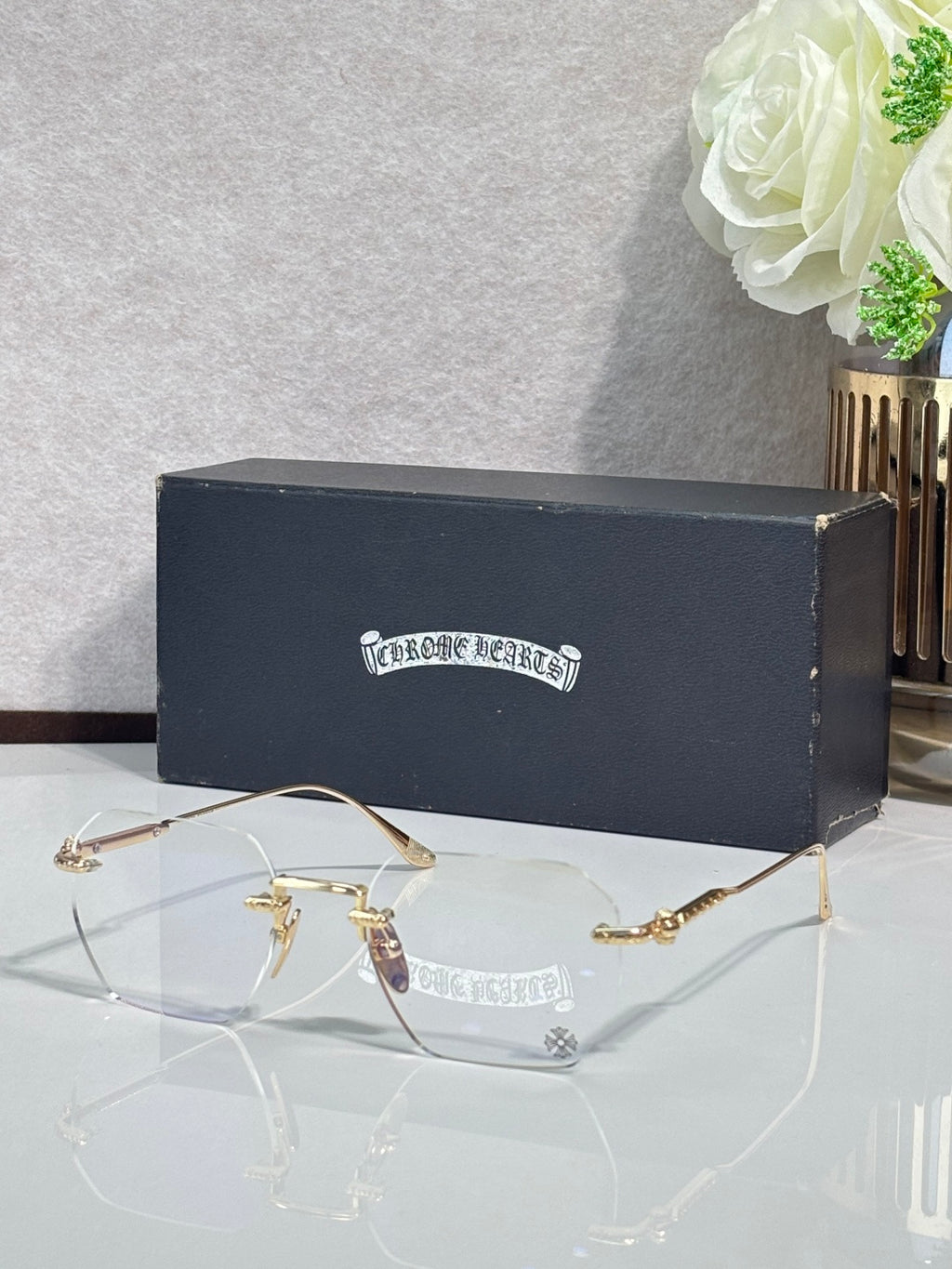Gold metal eyeglasses with clear lenses and small round logo on temple