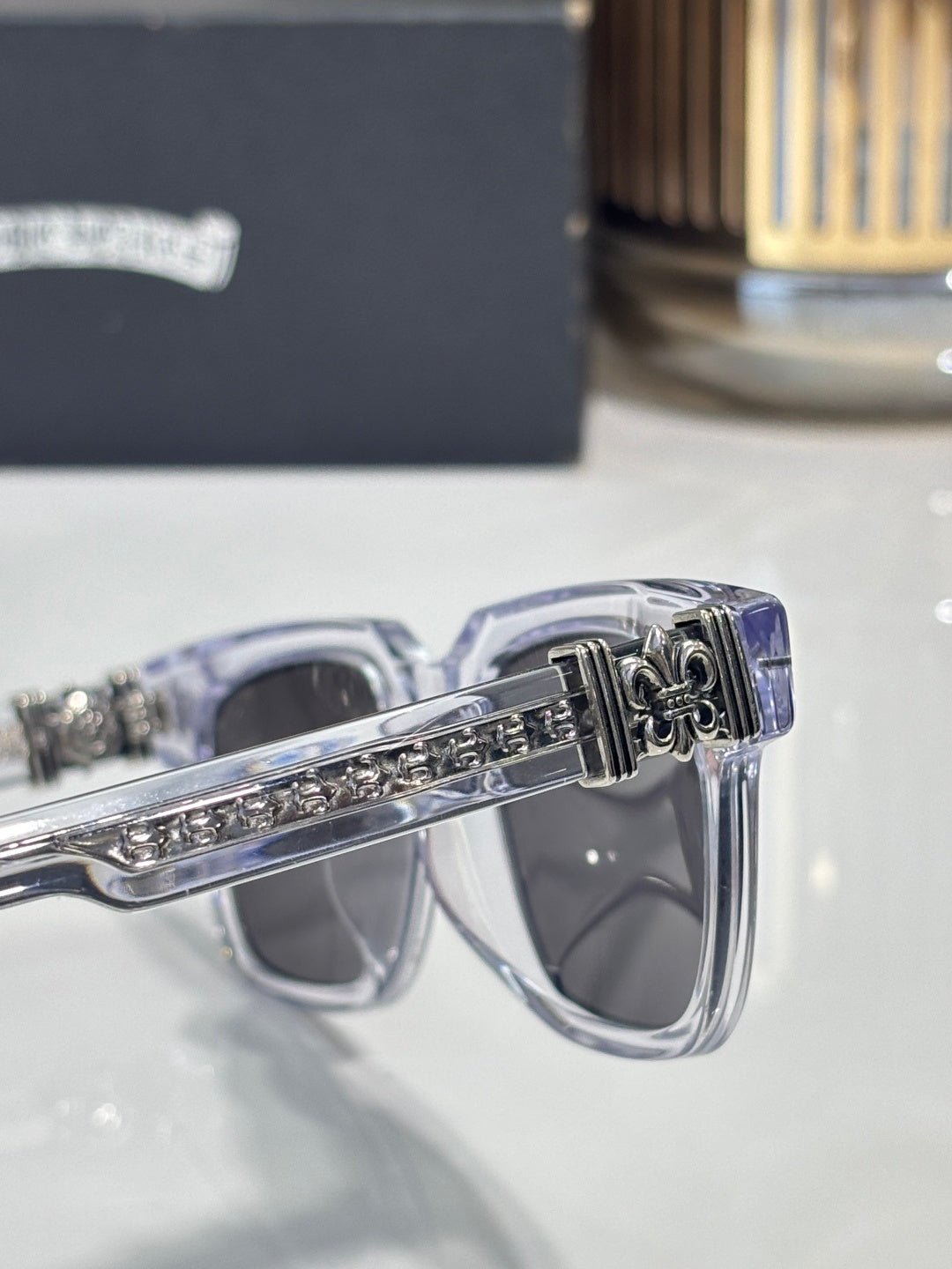 Chrome sunglasses temple close-up with intricate engraving and metal fleur-de-lis