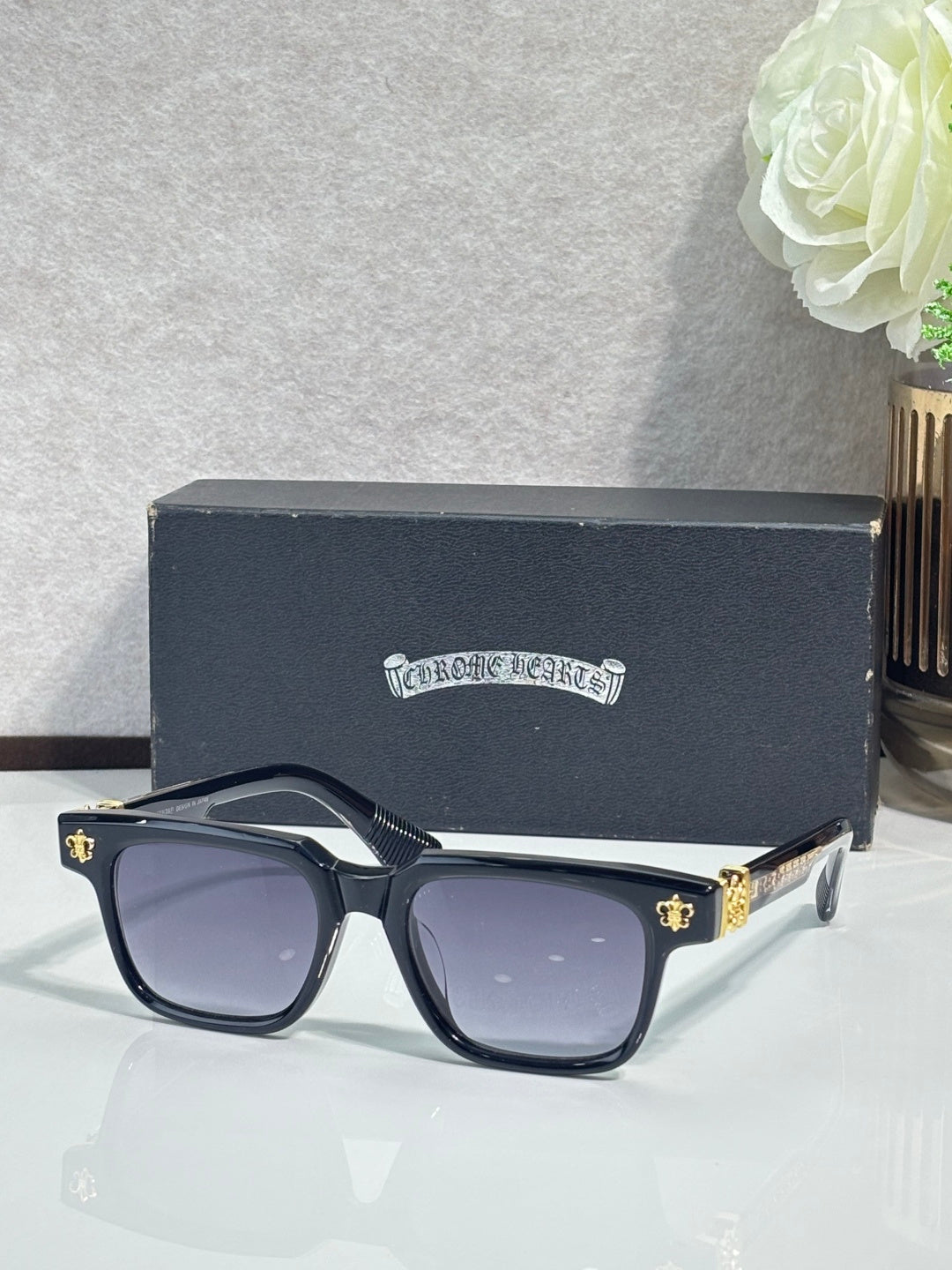 Dark blue-tinted sunglasses with chrome frame and gold fleur-de-lis hardware