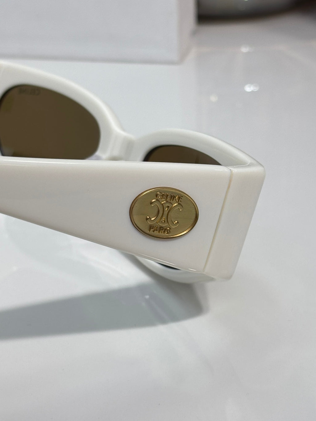 Celine sunglasses, white frame close-up with gold emblem on temple and brown lenses