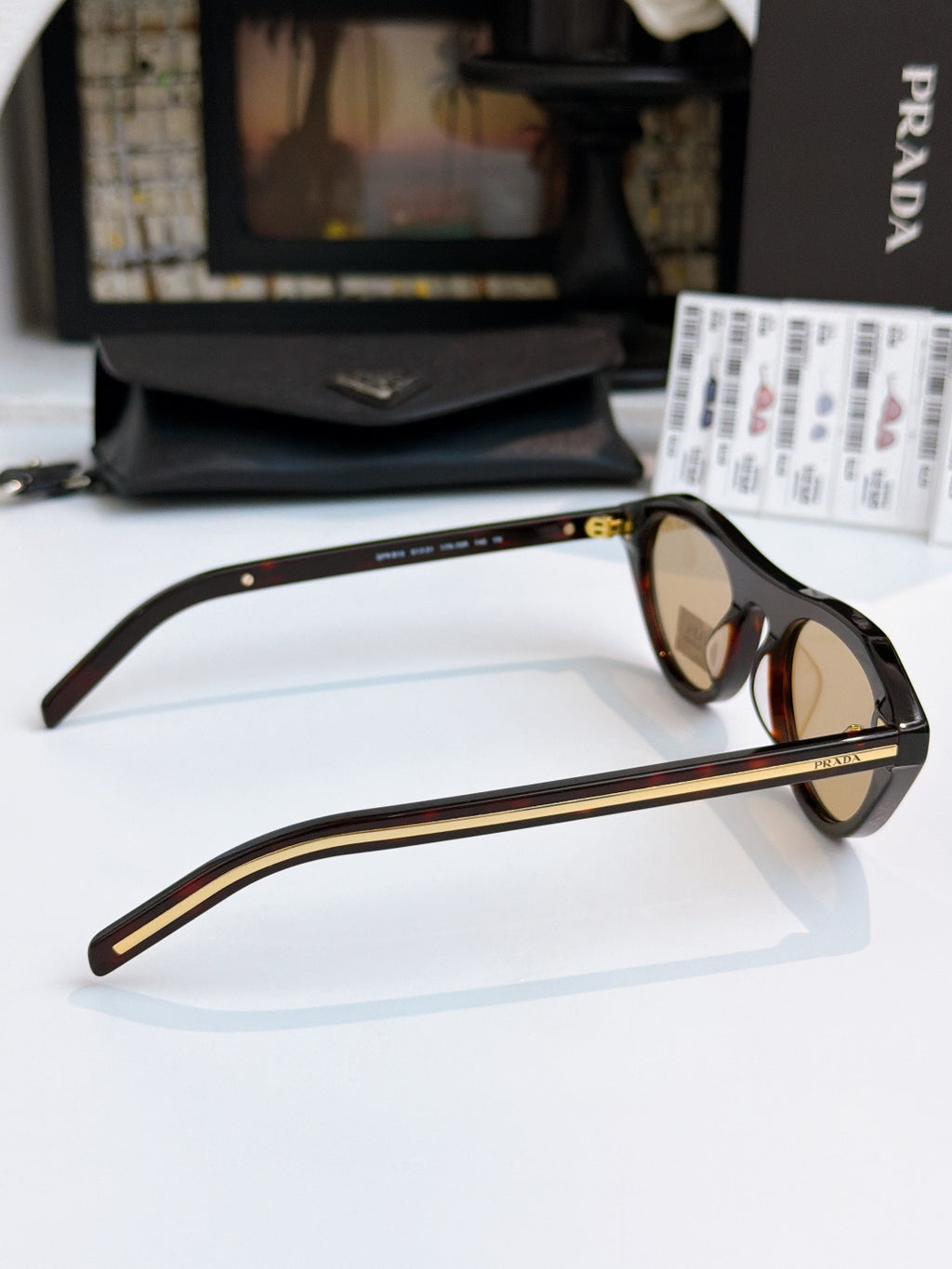 Prada sunglasses side view with black frames, tan lenses, and gold temple accents.