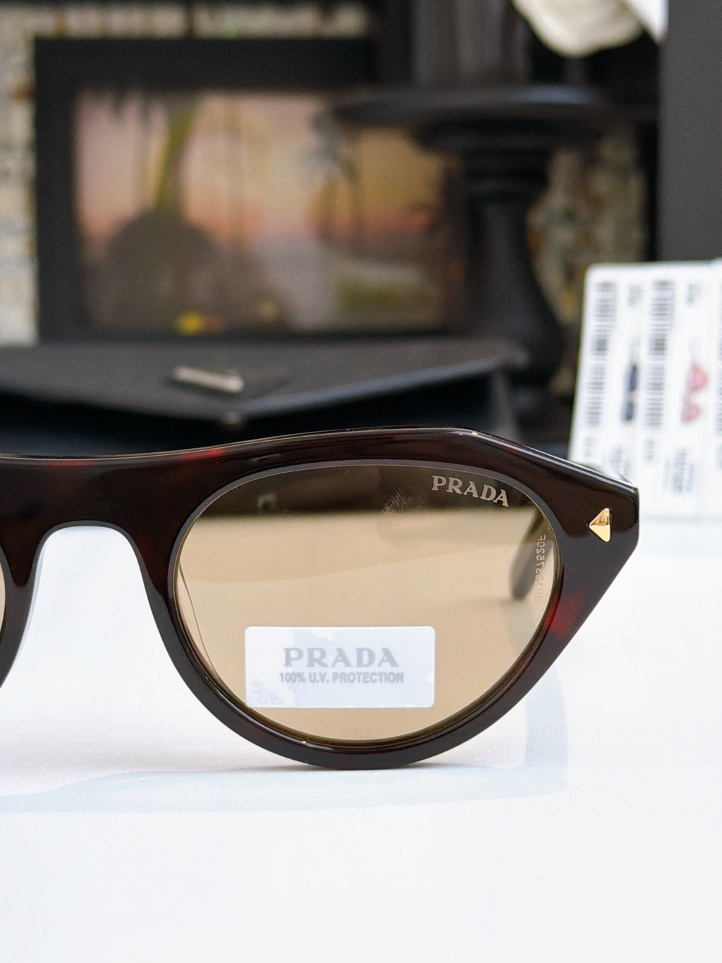 Prada sunglasses close-up with black frames and tan-tinted lenses, Prada logo on lens.