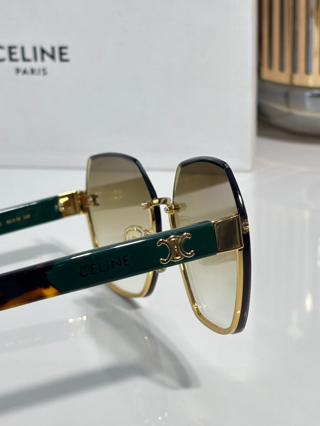 Celine sunglasses close-up: gold frame with dark green temple and logo bar
