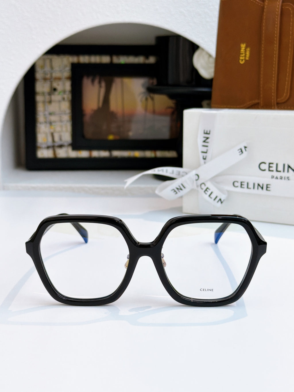 Black square eyeglass frames with light gray lenses, gold hinge detail.