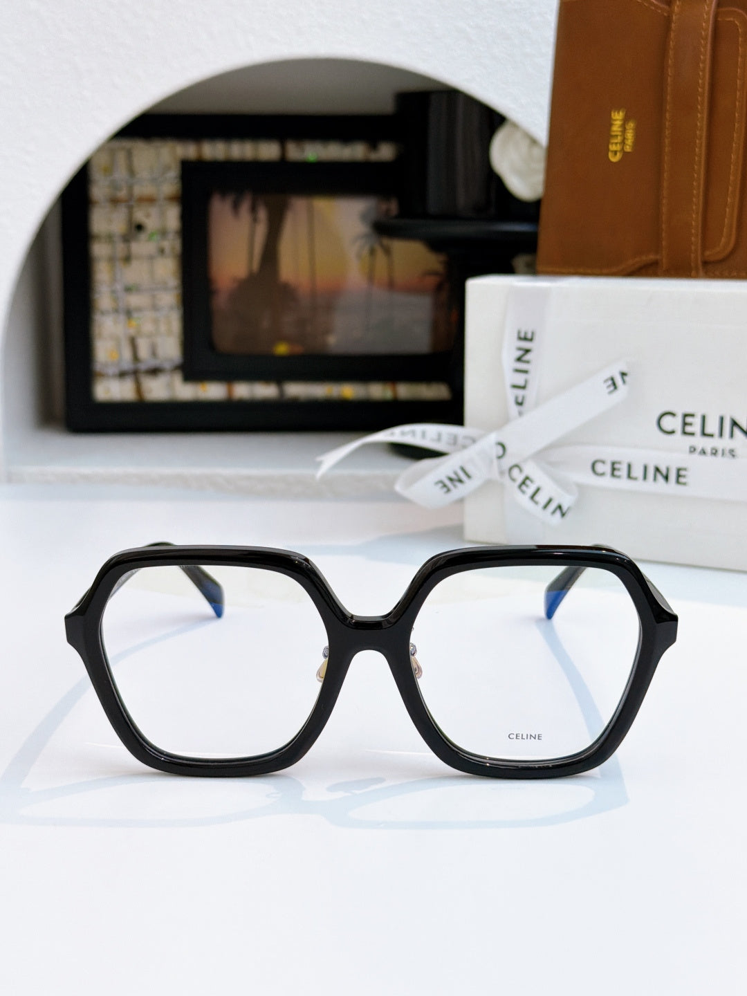 Black square eyeglass frames with light gray lenses, gold hinge detail.