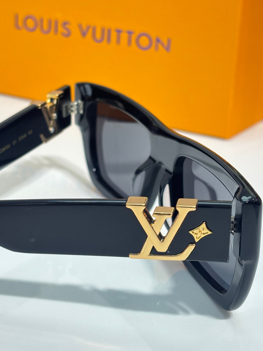 Louis Vuitton sunglasses close-up: gold LV emblem on dark temple