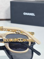 Sunglasses close-up with cream frames, gold chain detail, and dark lenses