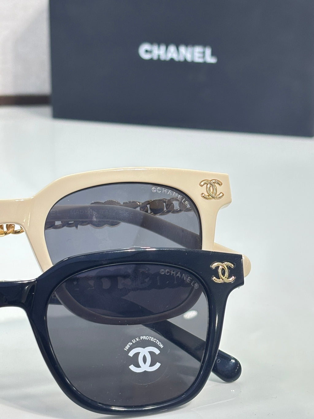 Pair of sunglasses with cream and black frames, gold chain accents, and dark lenses
