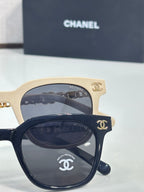 Pair of sunglasses with cream and black frames, gold chain accents, and dark lenses