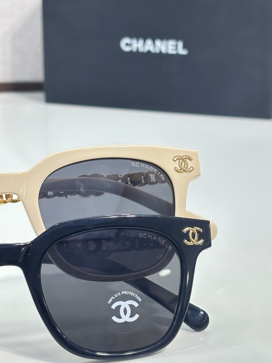 Pair of sunglasses with cream and black frames, gold chain accents, and dark lenses
