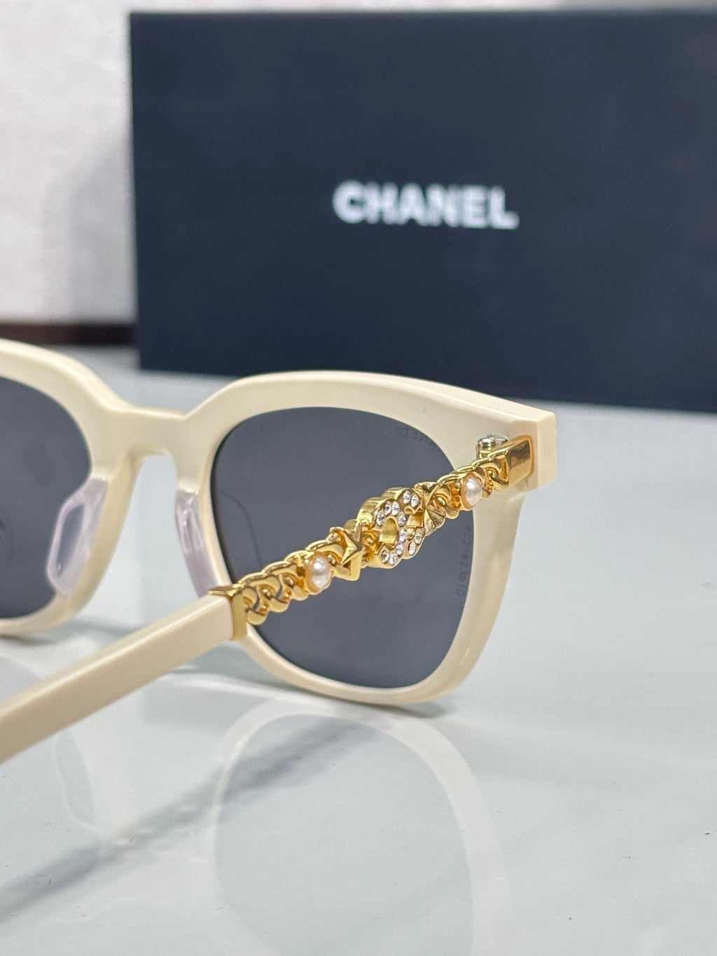 Sunglasses close-up: cream frames with gold chain detail on temple and dark lenses