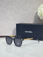 Sunglasses with dark frames, gold chain temple detail, and dark lenses
