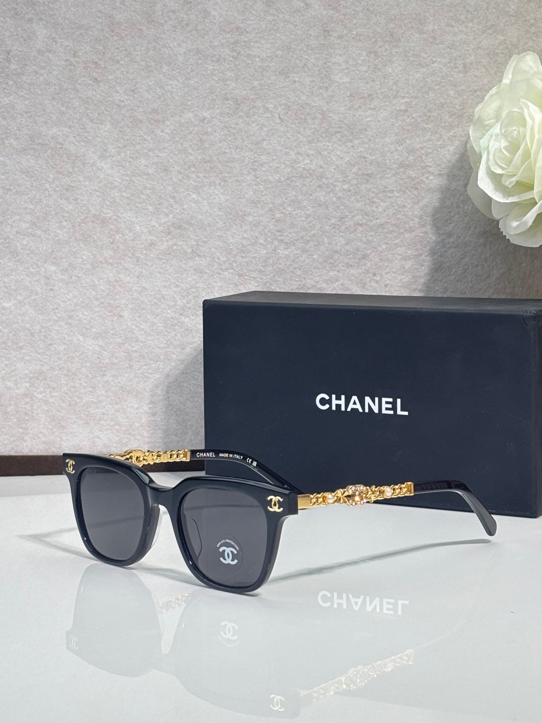 Sunglasses with dark frames, gold chain temple detail, and dark lenses
