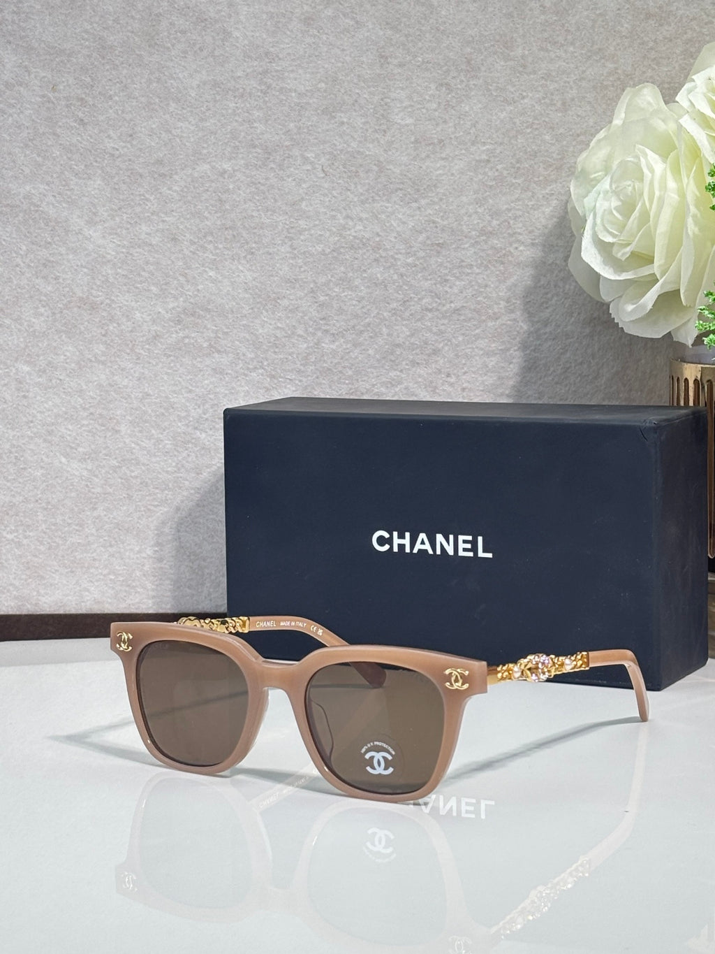 Sunglasses with brown frames, gold chain temple detail, and dark lenses
