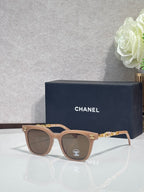 Sunglasses with brown frames, gold chain temple detail, and dark lenses