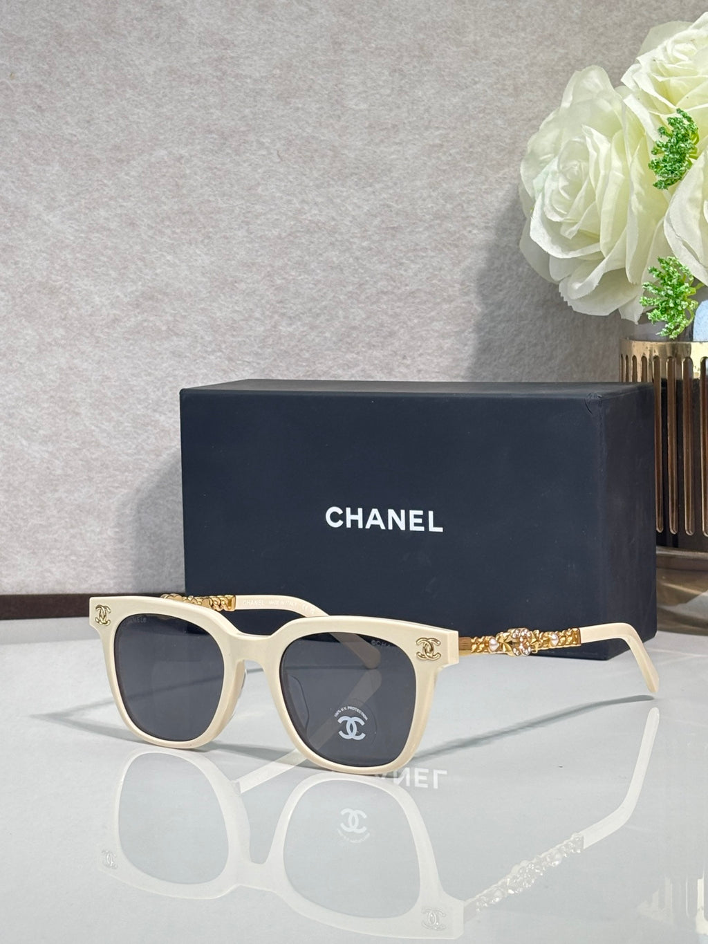 Sunglasses with cream frames, gold chain detail on temples, and dark lenses