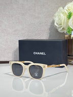 Sunglasses with cream frames, gold chain detail on temples, and dark lenses